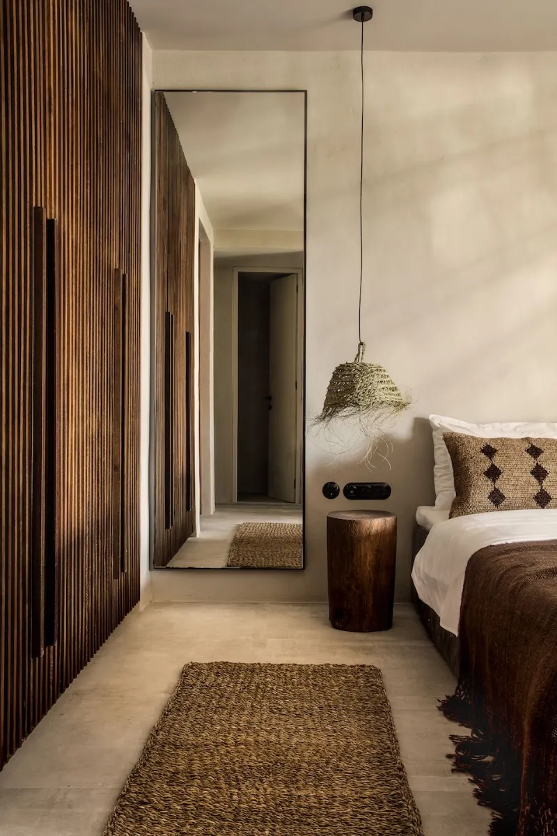 Chambre avec paroi en tasseaux de bois, suspension en rotin et chevet en bois brut