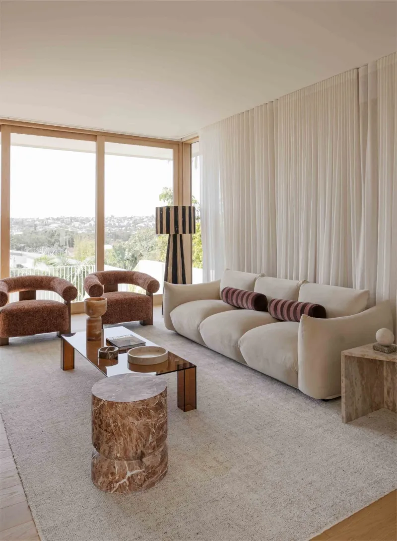 Salon lumineux face à la vue : canapé crème, fauteuils bouclette et table en bois